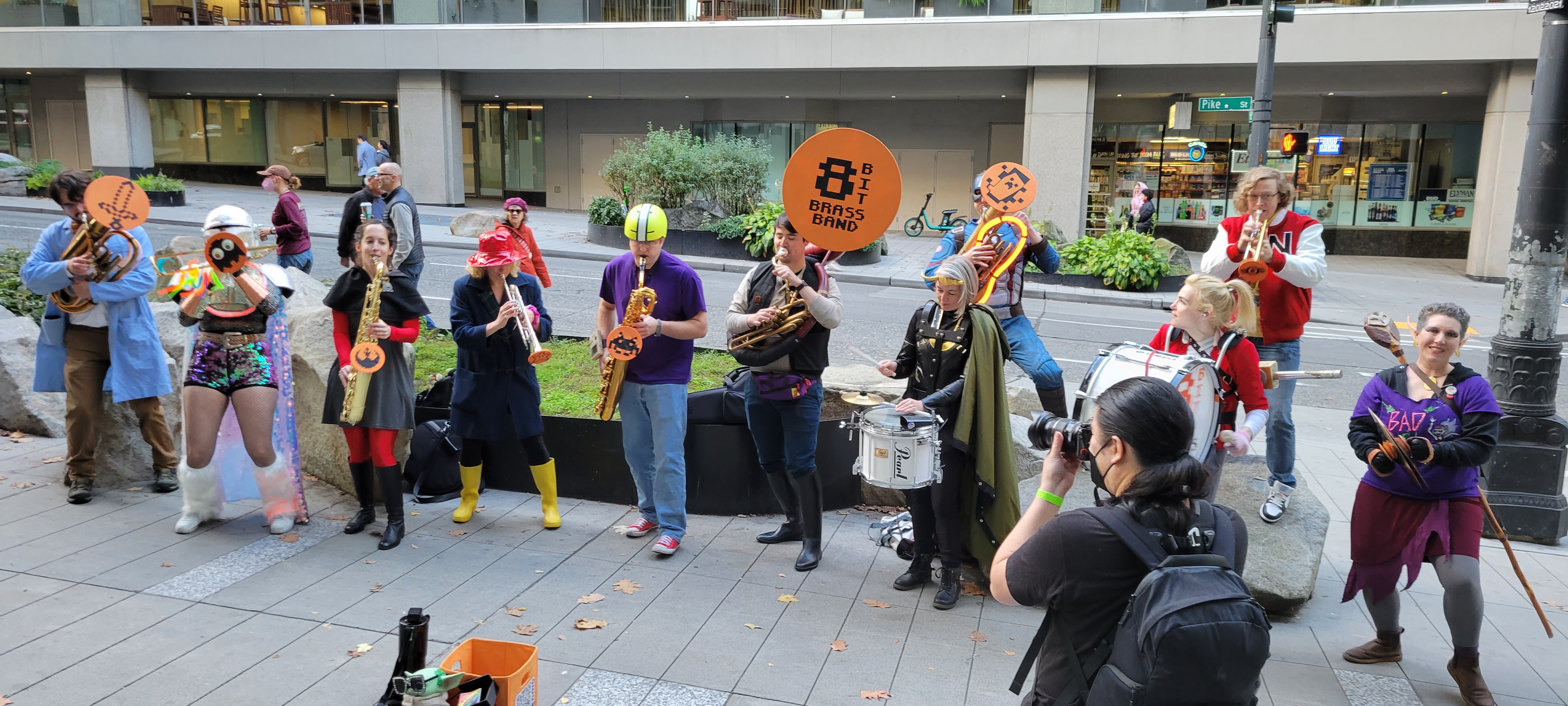 caption: Photographer Danny Ngan shoots the 8 Bit Brass Band on the sidewalk outside of GeekGirlCon 2022