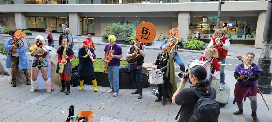 caption: Photographer Danny Ngan shoots the 8 Bit Brass Band on the sidewalk outside of GeekGirlCon 2022