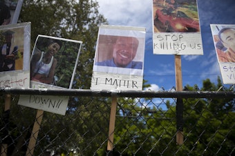 caption: FILE: A photograph of Manuel Ellis, center, is displayed on a fence along with other Black Americans who were unjustly killed by police officers ahead of the We Want to Live march for Black lives on Sunday June 7, 2020, at Othello Park in Seattle. Ellis was killed by Tacoma police officers on March 3rd.