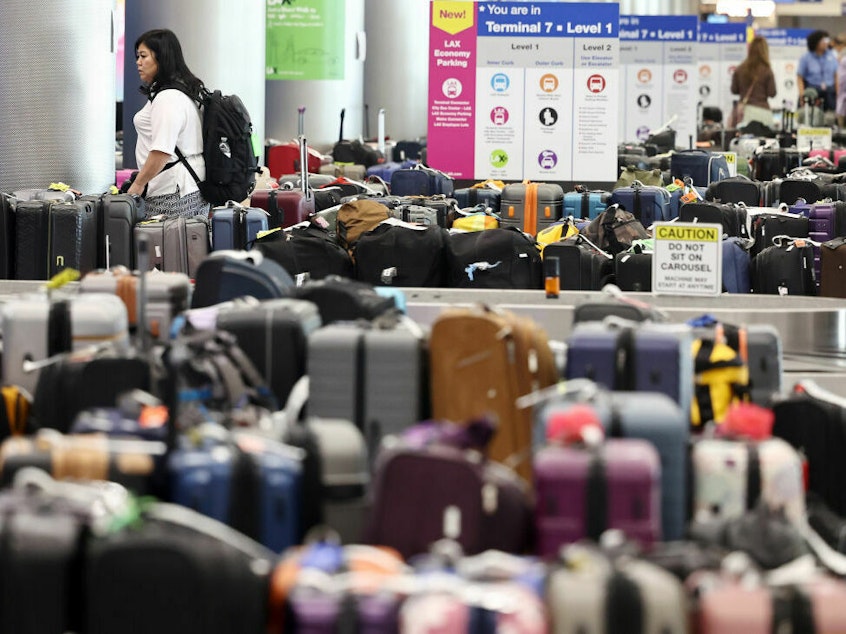 caption: A traveler looks for baggage amid rows of unclaimed luggage at Los Angeles International Airport in June.