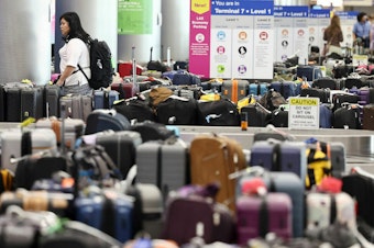 caption: A traveler looks for baggage amid rows of unclaimed luggage at Los Angeles International Airport in June.