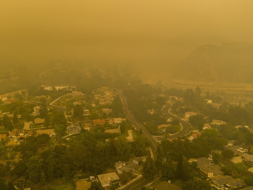 caption: Climate change has been a key factor in increasing the risk and extent of wildfires and other catastrophic weather events. Here, an aerial view shows neighborhoods in Monrovia, Calif., shrouded in smoke from the Bobcat Fire in September.