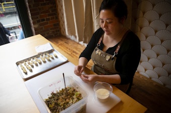 caption: Sara Upshaw, owner of OHSUN Banchan Deli & Cafe, makes dumplings on Tuesday, Feb. 6, 2024, at the restaurant in Seattle’s Pioneer Square neighborhood. 