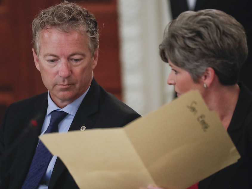 caption: Sen. Rand Paul, R-Ky., performed the Heimlich maneuver on Sen. Joni Ernst, R-Iowa as she was choking Thursday during a closed-door GOP lunch. Here, Paul and Ernst look over a folder provided to them by the White House, during a luncheon in 2017 in the State Dinning Room of the White House.