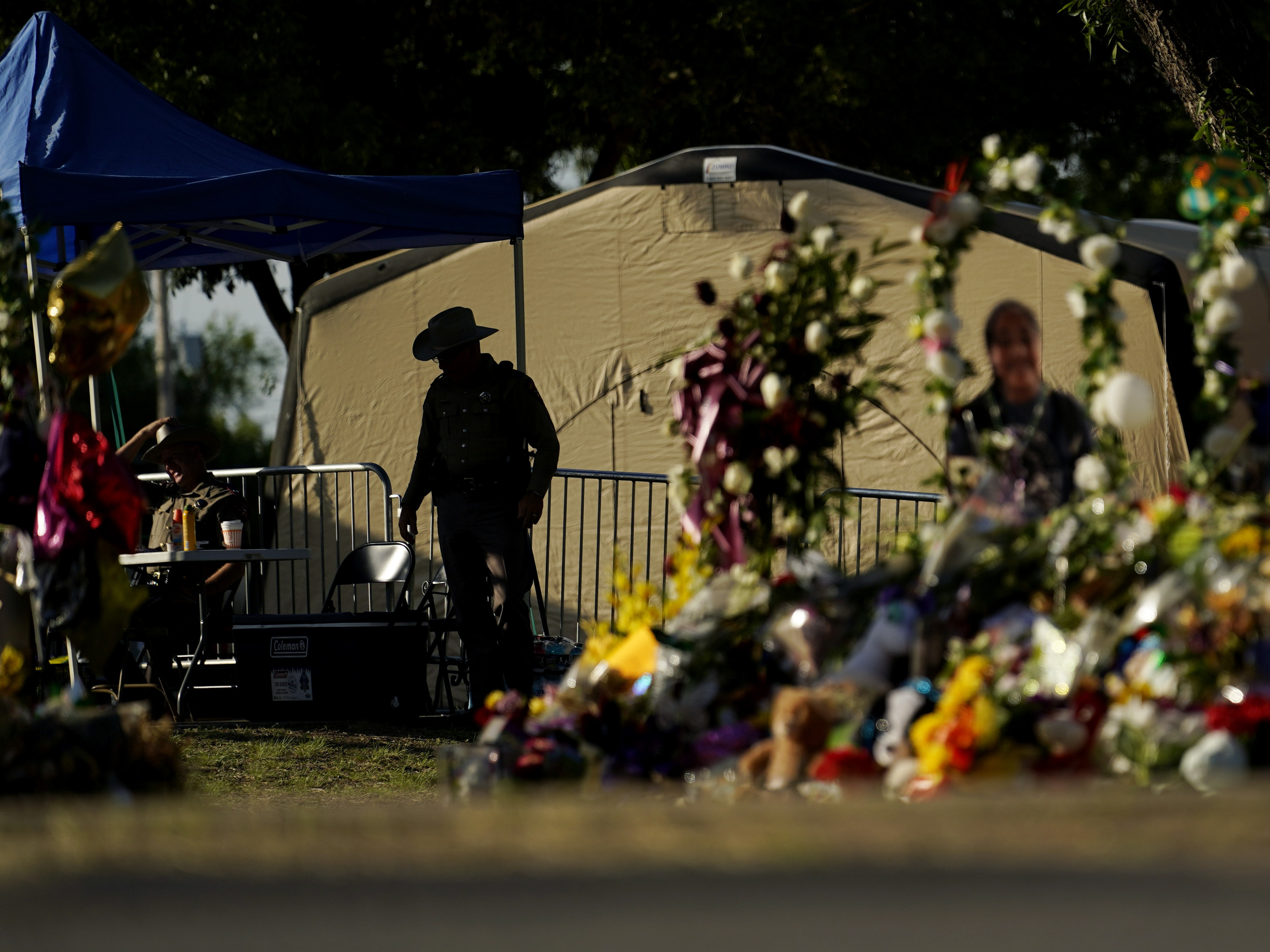 caption: A Texas Department of Public Safety officer keeps watch on June 3, 2022, in Uvalde, Texas, near a memorial outside Robb Elementary School.