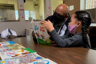 caption: Gerald  Donaldson, a family support worker at Leschi Elementary in Seattle, reads to a kindergartener at a youth center during the Covid-19 pandemic.