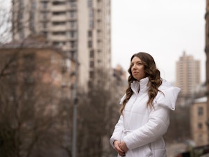 caption: Lytvynova stands near an apartment building in her Kyiv neighborhood that was damaged by multiple Russian strikes over the course of the war.