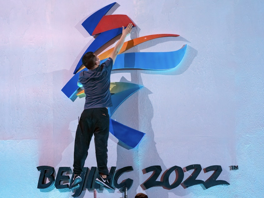 caption: A crew member leaps to fix a logo for the 2022 Winter Olympics in Beijing earlier this month. The International Olympic Committee says it will allow fans from mainland China to attend the competition in person.