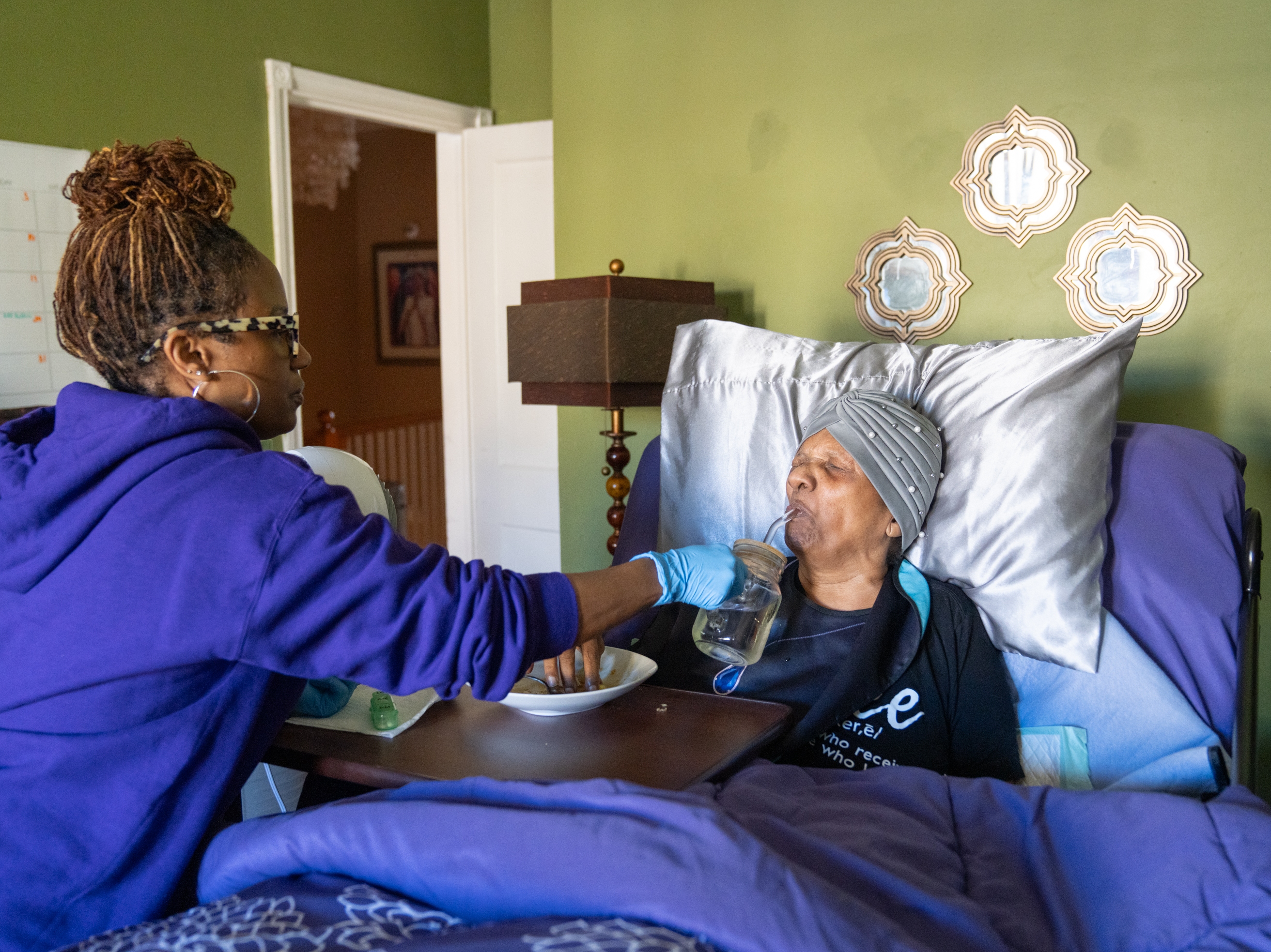 caption: Dawnita Brown gives her mother, Joan Cain, water to help swallow pills after breakfast. Brown is the primary caregiver to her mother and father, who live with her in Baltimore.
