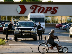 caption: A cyclist pauses passes the scene of a shooting at a supermarket, in Buffalo, N.Y., Sunday, May 15, 2022.