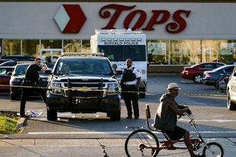 caption: A cyclist pauses passes the scene of a shooting at a supermarket, in Buffalo, N.Y., Sunday, May 15, 2022.