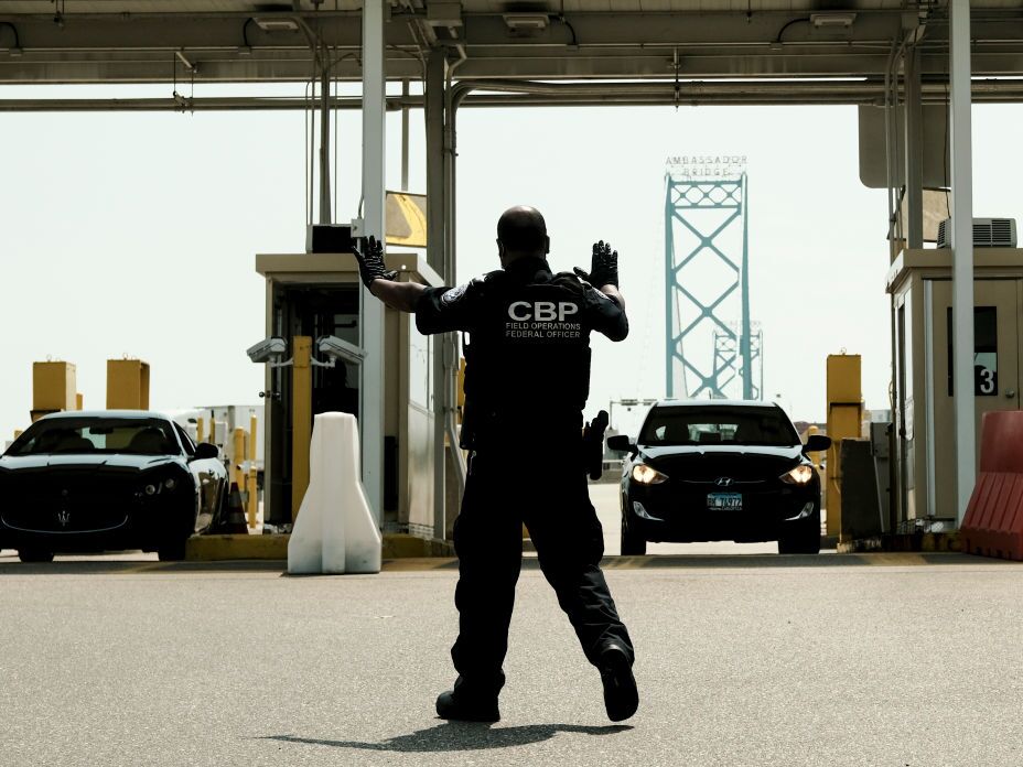 caption: U.S. Customs and Border Protection agents direct vehicles re-entering the U.S. from Canada at the Ambassador Bridge Port of Entry in Detroit.