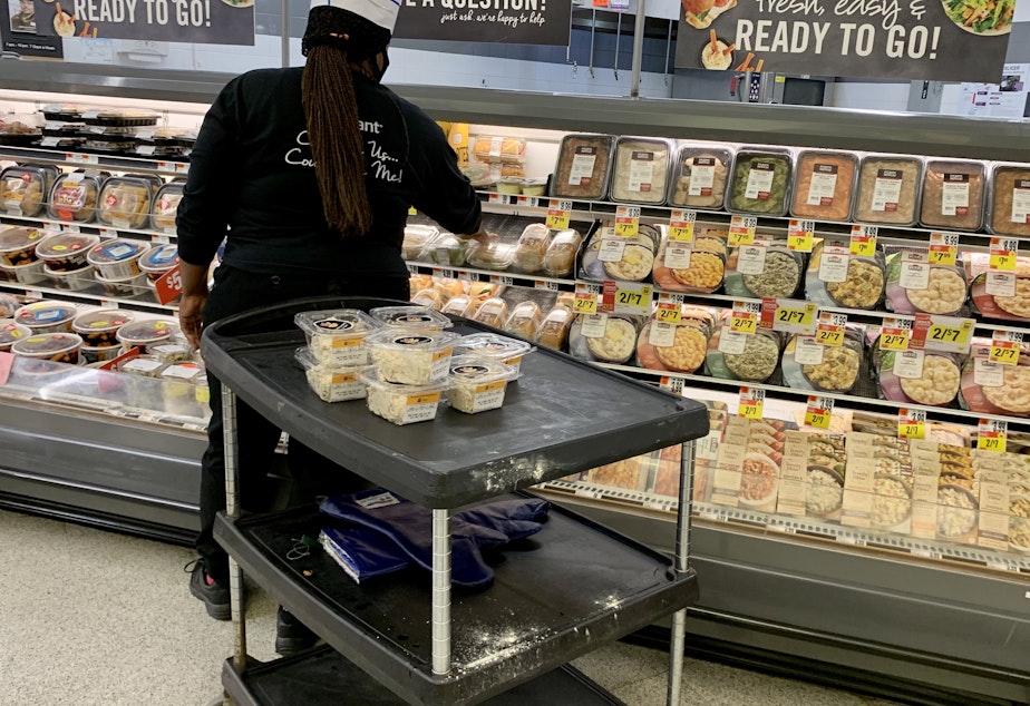 caption: Grocery prices have fallen in recent months but are still 4.6% higher than at this time last year. Here, a woman stock shelves in a deli in June at a Washington, D.C., supermarket.