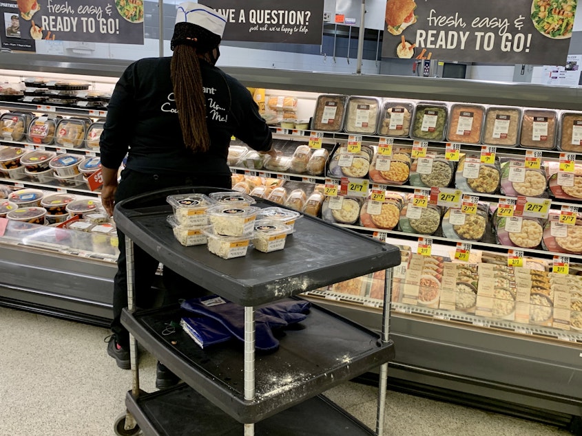 caption: Grocery prices have fallen in recent months but are still 4.6% higher than at this time last year. Here, a woman stock shelves in a deli in June at a Washington, D.C., supermarket.