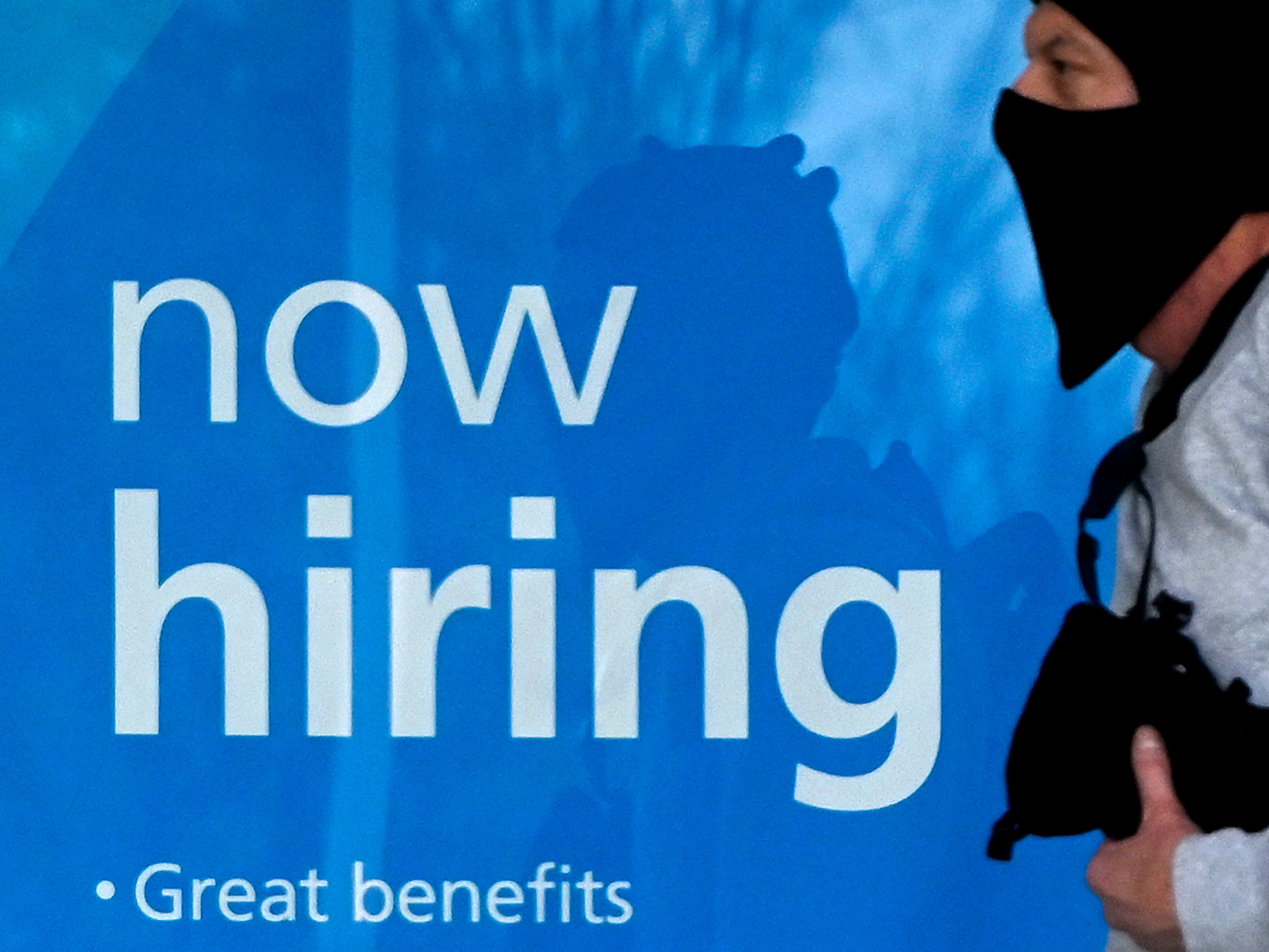 caption: A man wearing a face mask walks past a "Now Hiring" sign in front of a store on Jan. 13, in Arlington, Va. The labor market is showing resilience despite a recent spike in omicron-related coronavirus infections.