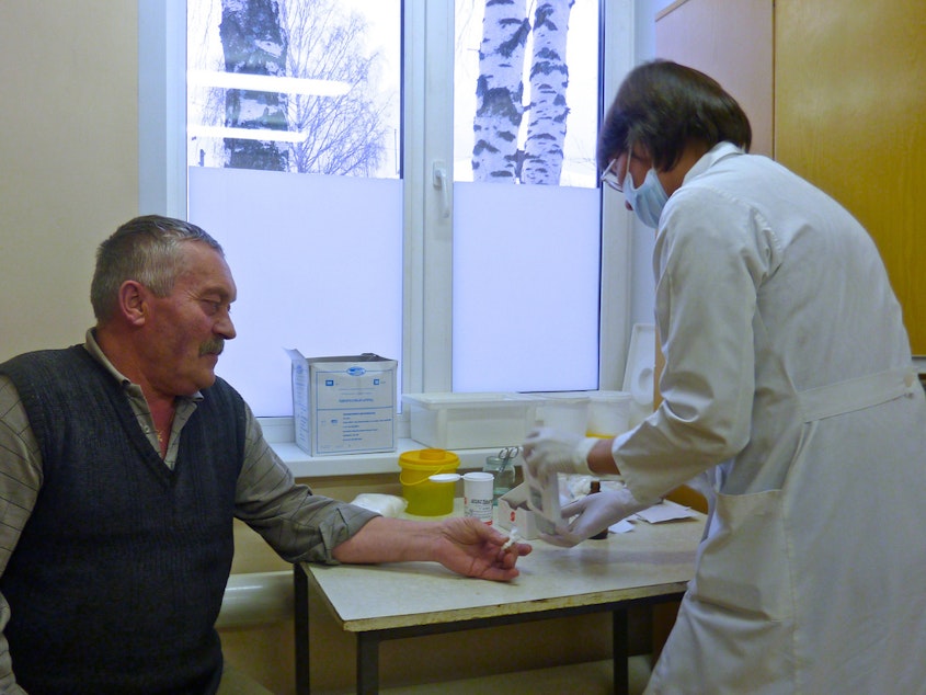 caption: A doctor takes a blood sample from an older patient.