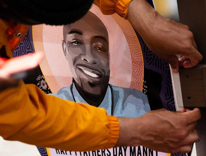 caption: Community members gathered in June for a celebration of life for Manuel Ellis, who was killed by Tacoma police in March. In this photo, one of the attendees hangs a flyer that says 'Happy Father's Day Manny'