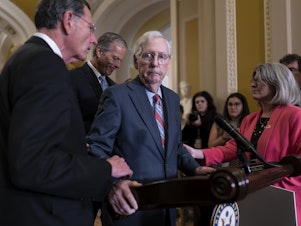 caption: Senate Minority Leader Mitch McConnell, R-Ky., center, is helped by, from left, Sen. John Barrasso, R-Wyo., Sen. John Thune, R-S.D., and Sen. Joni Ernst, R-Iowa, after the 81-year-old GOP leader froze at the microphones as he arrived for a news conference, at the Capitol in Washington on July 26.