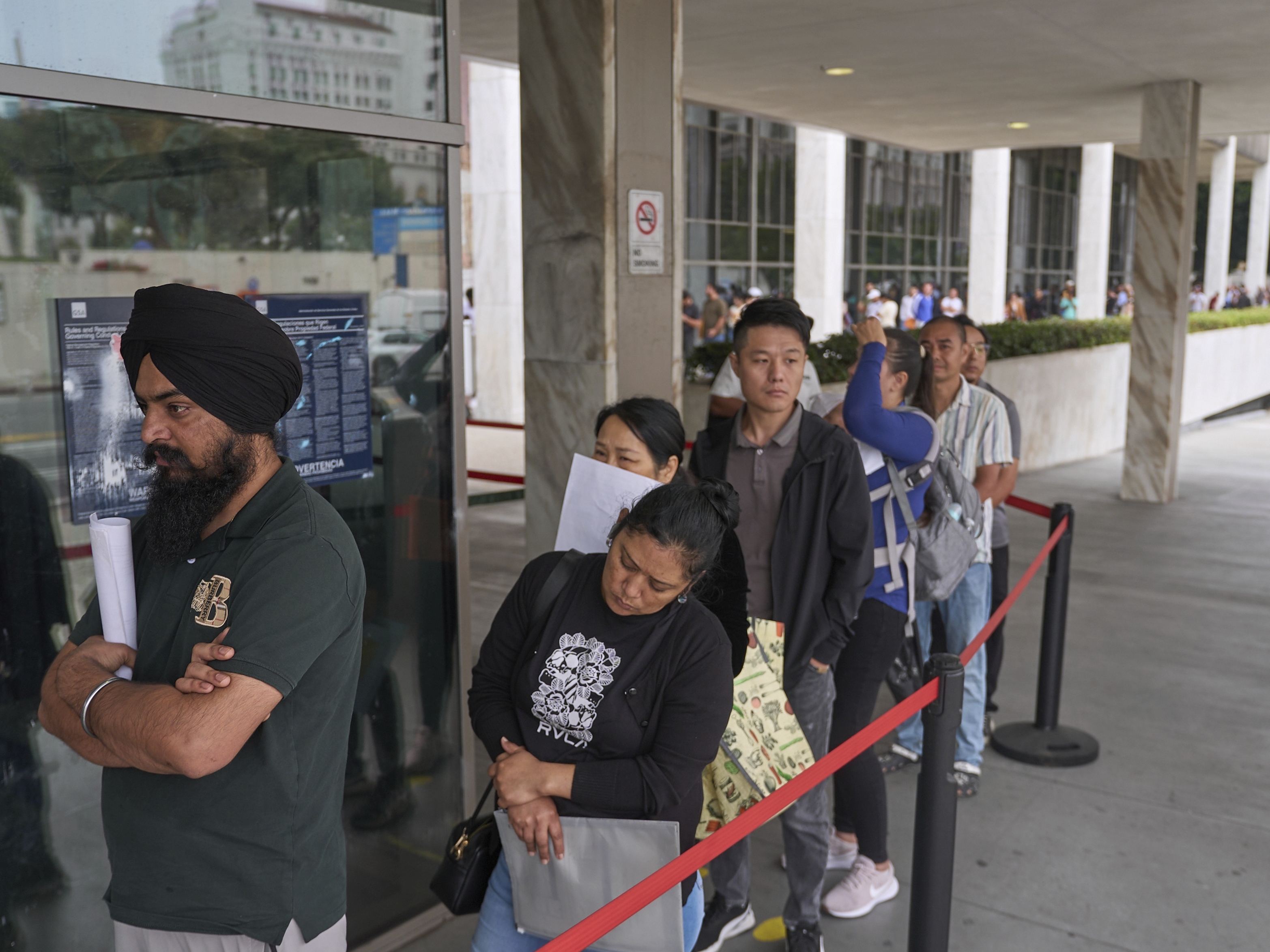 caption: In June 2025, people line up outside the Los Angeles Federal Building, which houses offices for U.S. Immigration and Customs Enforcement and U.S. Citizenship and Immigration Services.