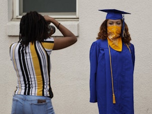 caption: Anderson High School senior Teyaja Jones, right, poses in her cap and gown and a bandana face cover, Tuesday, May 5, 2020, in Austin, Texas.