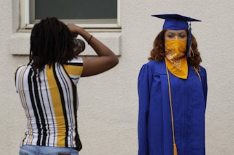 caption: Anderson High School senior Teyaja Jones, right, poses in her cap and gown and a bandana face cover, Tuesday, May 5, 2020, in Austin, Texas.