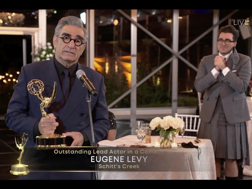 caption: Eugene Levy accepts his award for lead actor in a comedy series for <em>Schitt's Creek </em>as his son (and creative partner) Dan Levy looks on at Sunday night's Emmy Awards.