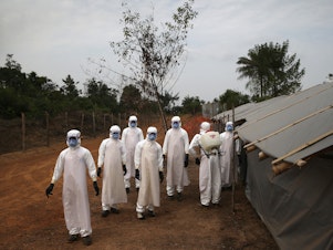 caption: A burial team in Liberia awaits decontamination after performing "safe burials" for people who died of Ebola during the 2014-15 outbreak. Strains of the virus are harbored by bats and primates. A new study looks at how human activity affects the transmission of infectious diseases like Ebola.