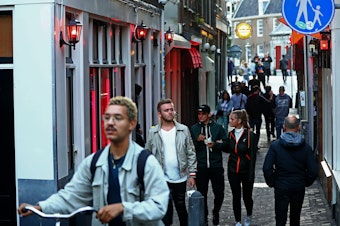 caption: People walk through Amsterdam's red-light district shortly after it reopened in 2020, during the pandemic. The neighborhood attracts millions of tourists each year.