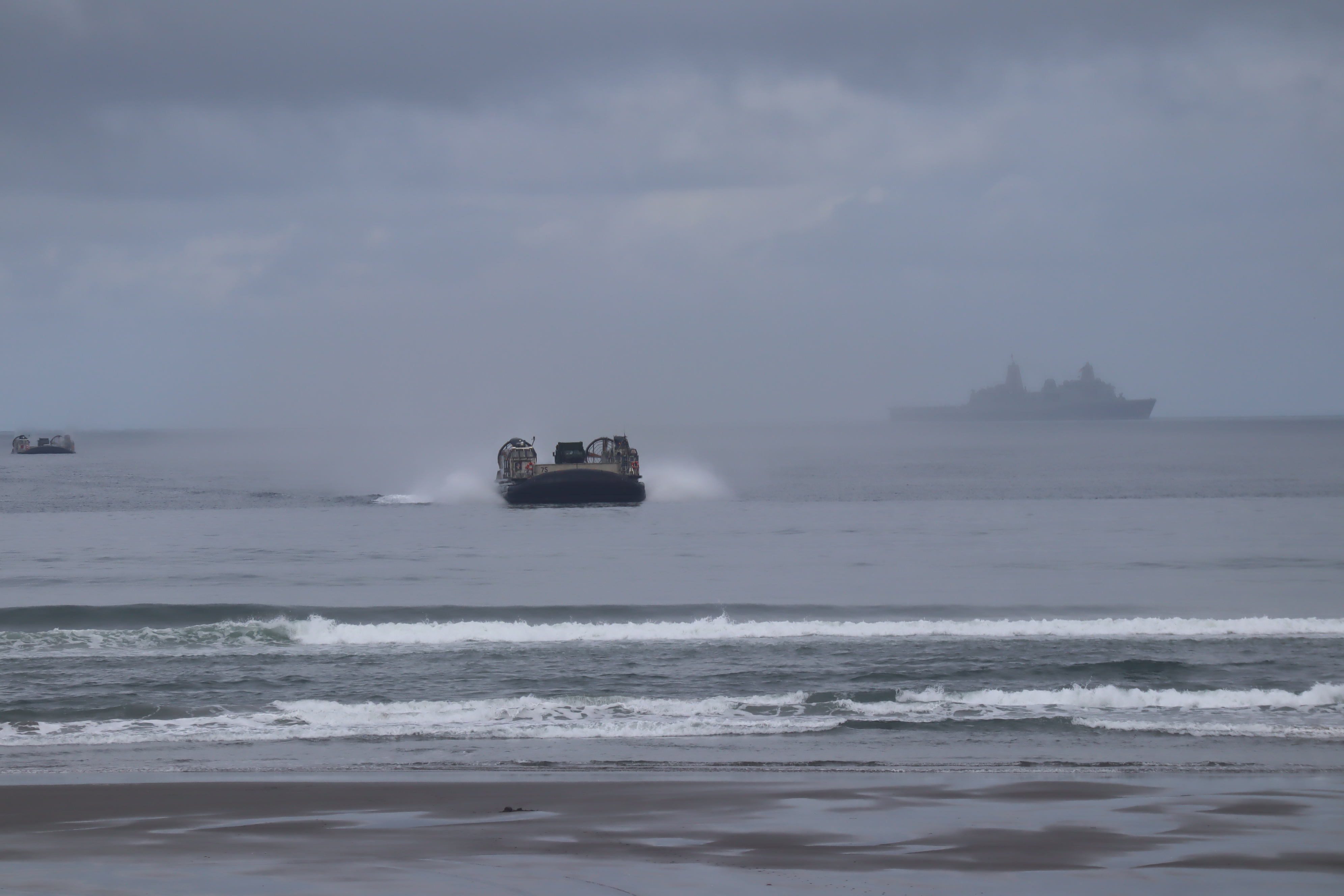 caption: The USS Anchorage, top right, launched two hovercraft to bring mock disaster relief supplies to shore Monday at Oregon's Sunset Beach State Recreation Site.