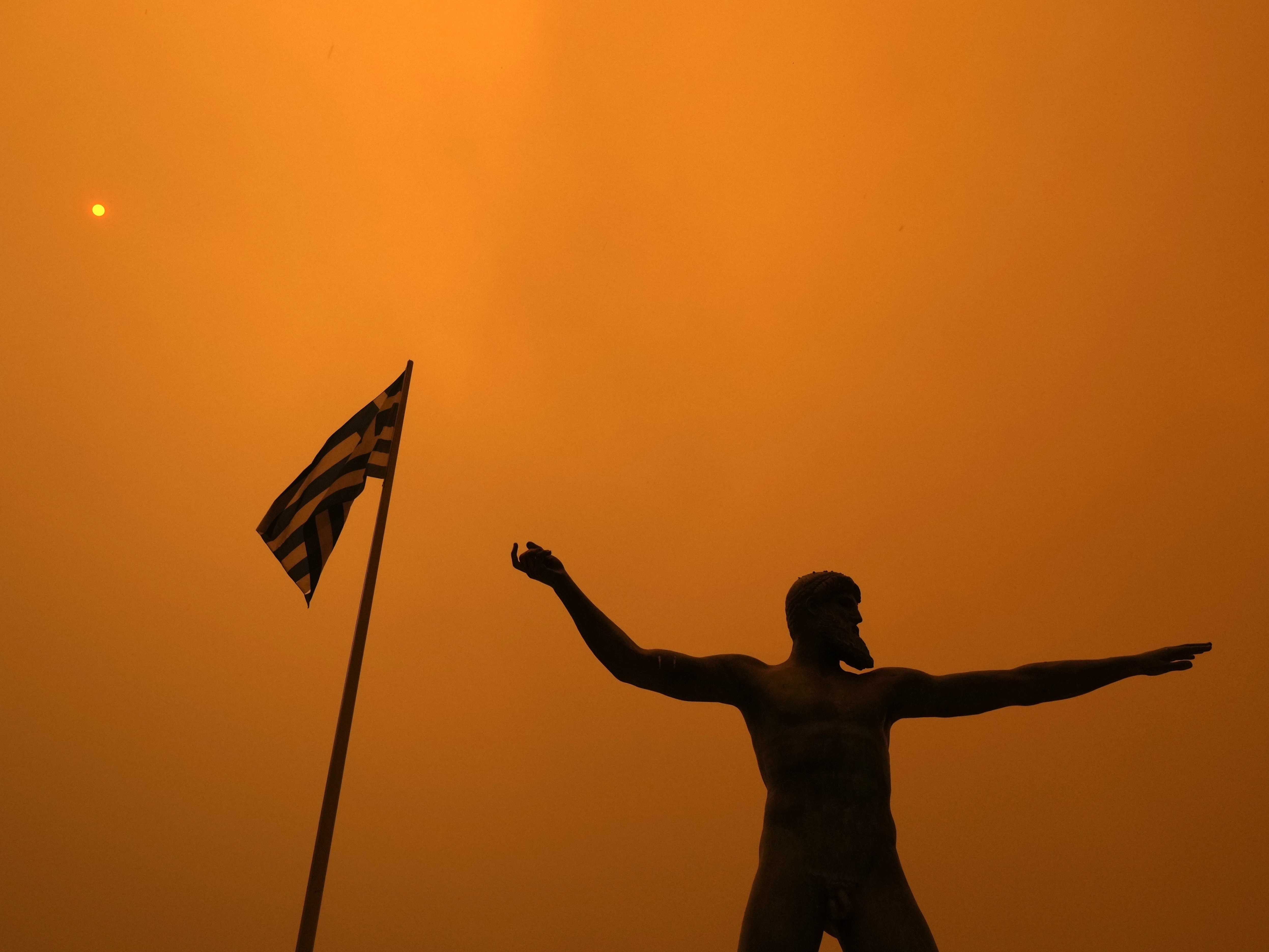 caption: Smoke from wildfire spreads Sunday over the statue of Poseidon, ancient Greek God of the sea, at Pefki village on Evia island, about 118 miles north of Athens.
