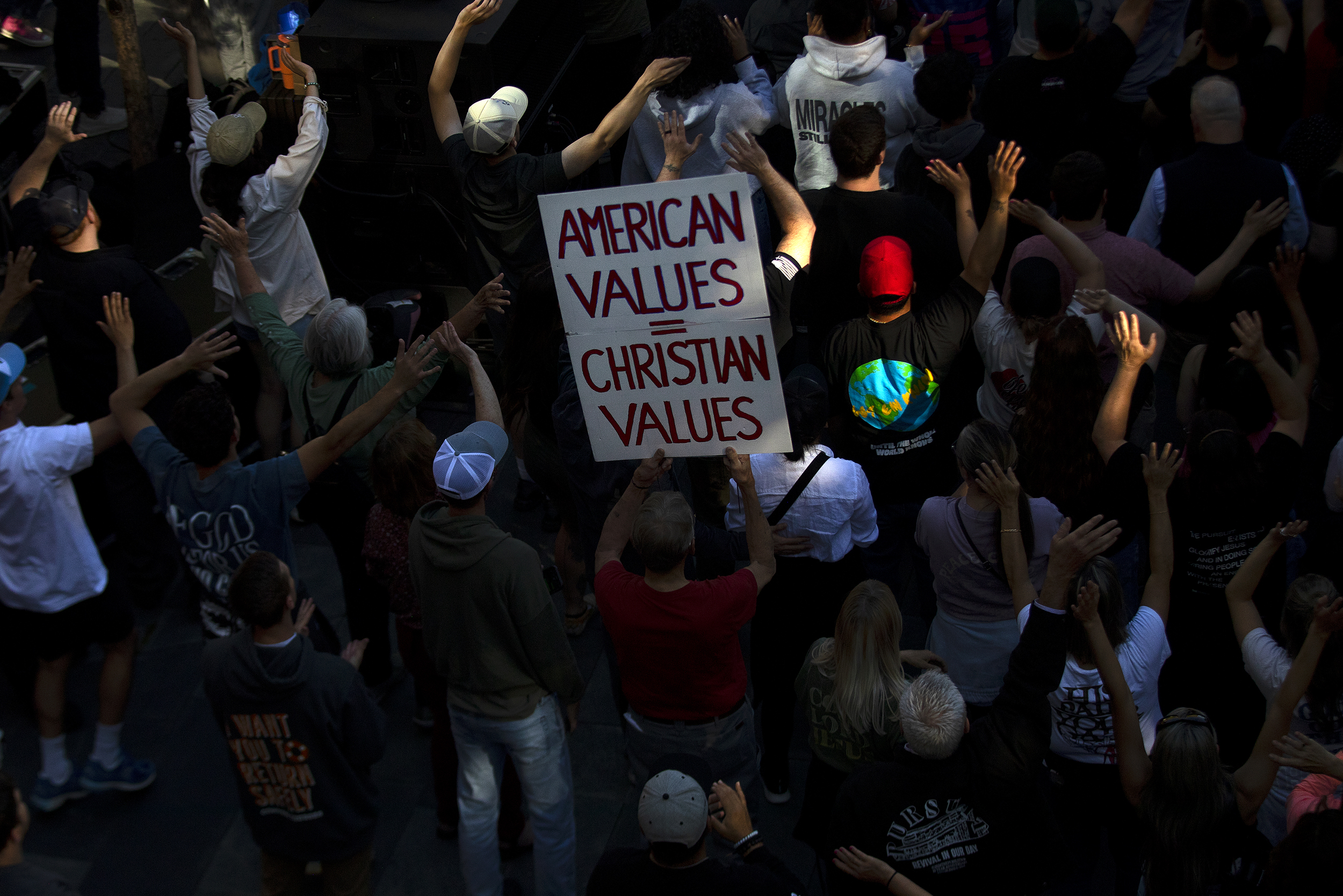 caption: 'American Values = Christian Values' reads a sign at the fundamentalist Christian group Mayday USA’s ‘Rattle in Seattle’ event, on Tuesday, May 27, 2025, outside of Seattle City Hall. Tuesday's event saw eight arrests as skirmishes between demonstrators with Mayday USA, a Christian fundamentalist group advocating against trans rights, and pro-LGBTQ activists from either side of a police barricade.