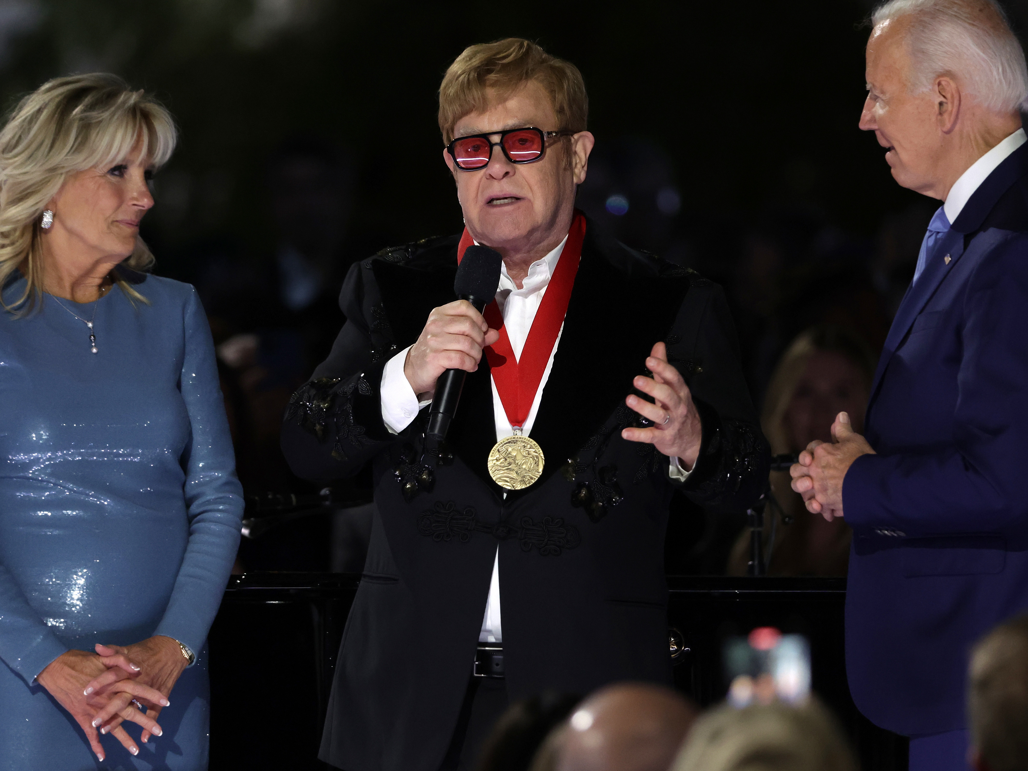 caption: Sir Elton John speaks after being presented with the National Humanities Medal by President Biden as first lady Jill Biden looks on during an event at the South Lawn of the White House on Friday.