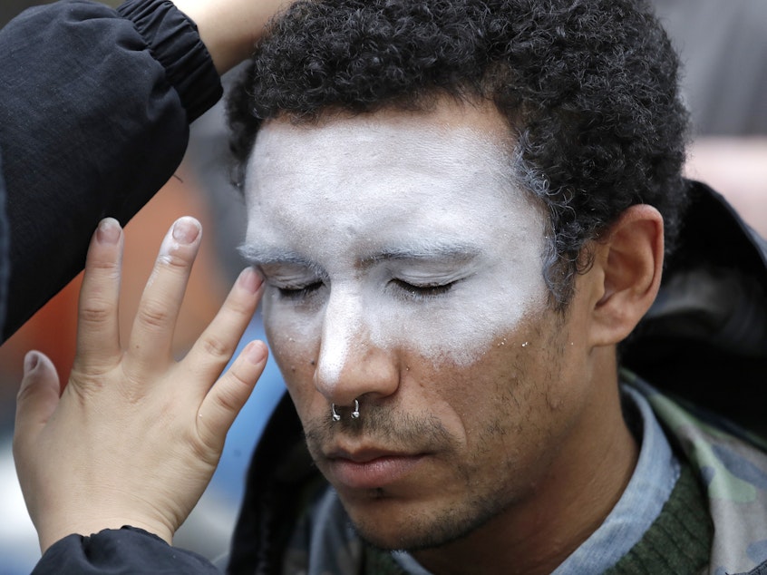 caption: In this Oct. 31 photo, a man has his face painted to represent efforts to defeat facial recognition. It was during a protest at Amazon headquarters over the company's facial recognition system.