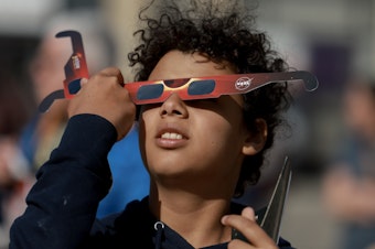 caption: Junior Espejo looks through eclipse glasses being handed out by NASA in Houlton, Maine. Used correctly, eclipse glasses prevent eye damage.