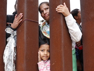 caption: A mother and daughter await volunteer assistance while stuck in a makeshift camp at the U.S.-Mexico border.