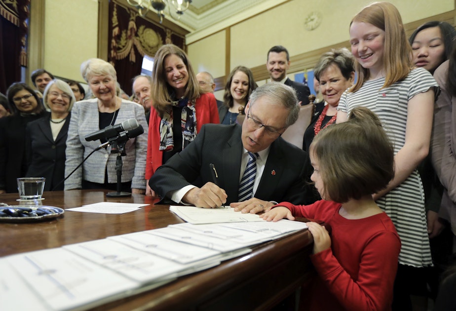 caption: Washington Gov. Jay Inslee, center, signs a measure at the Capitol in Olympia, Wash., Wednesday, March 21, 2018, that seeks to reduce the wage gap between men and women and provide equal growth opportunities and fair treatment in the workplace. 