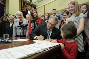 caption: Washington Gov. Jay Inslee, center, signs a measure at the Capitol in Olympia, Wash., Wednesday, March 21, 2018, that seeks to reduce the wage gap between men and women and provide equal growth opportunities and fair treatment in the workplace. 