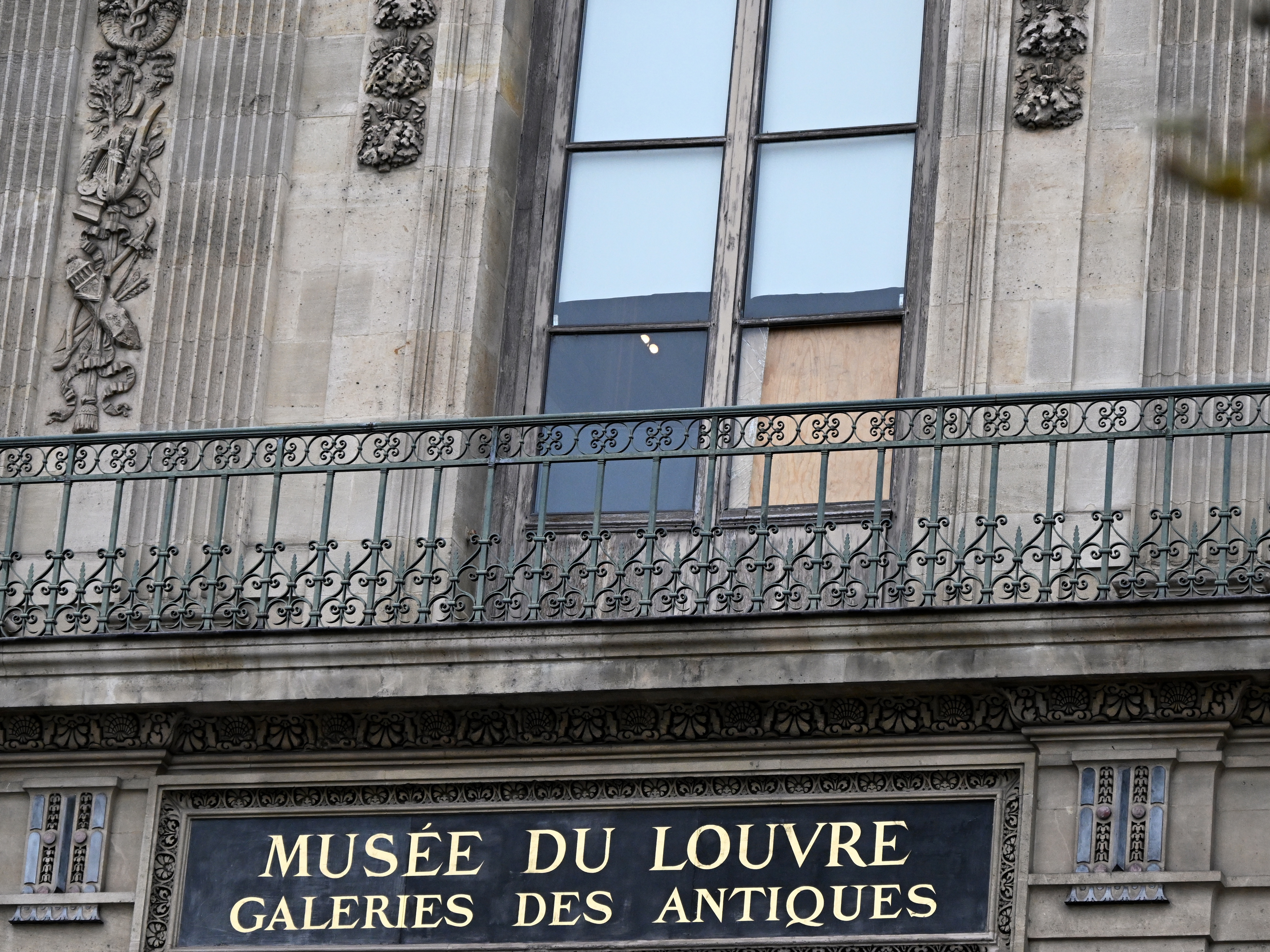 caption: A plywood board covers the window where thieves entered the Louvre museum to steal historic jewels.