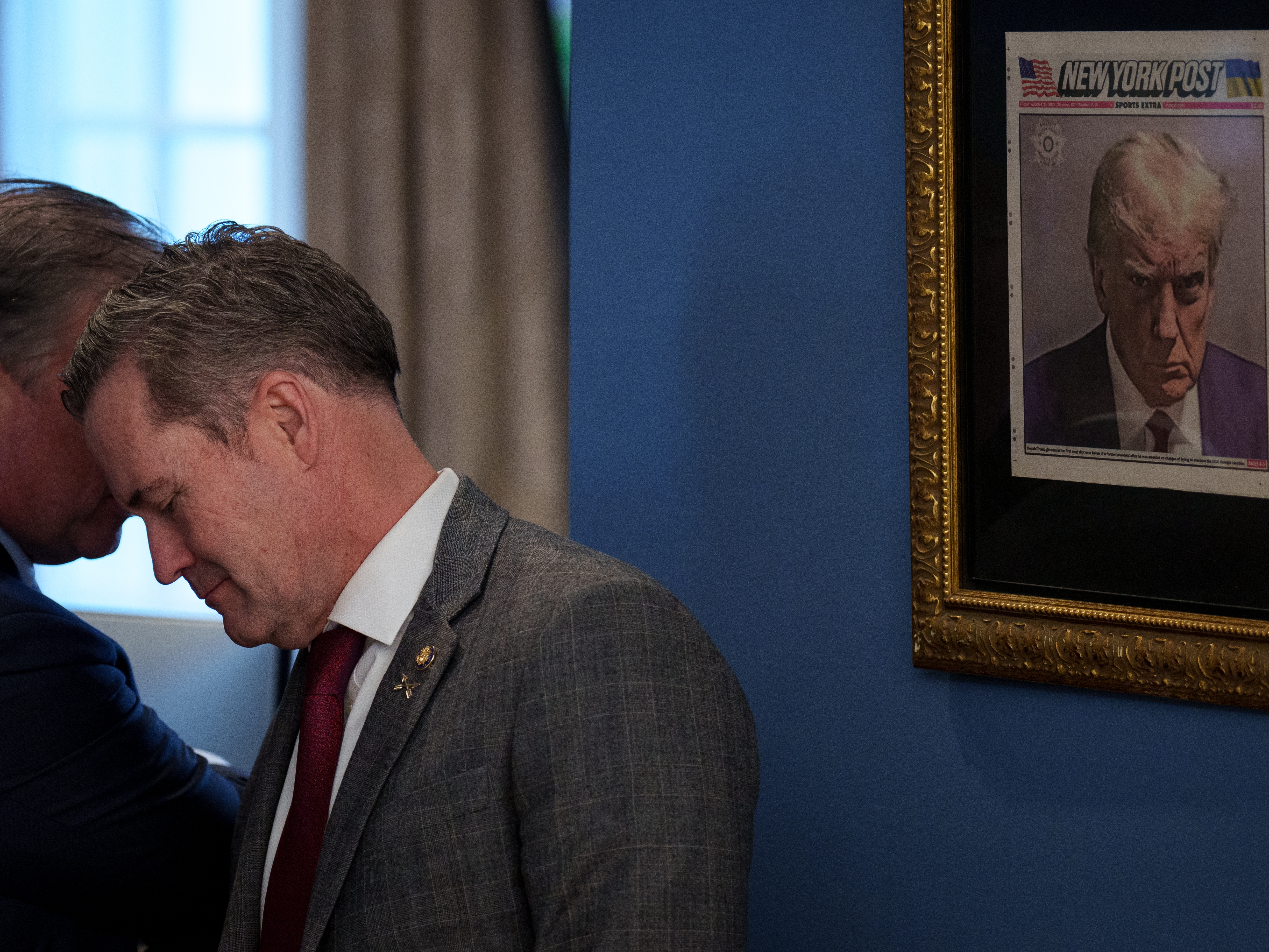 caption: In this file photo from Feb. 14, 2025, Mike Waltz speaks with an official just outside the Oval Office where a copy of President Trump's mugshot on the front page of the <em>New York Post</em> is posted.