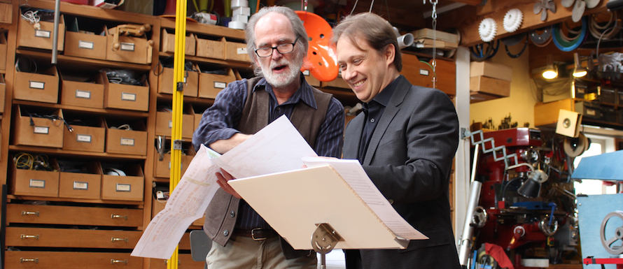 caption: The artist Trimpin and Seattle Symphony conductor Ludovic Morlot look over Trimpin's plans.