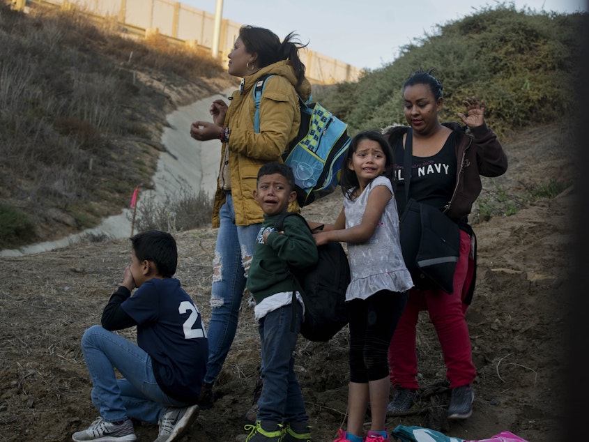 caption: Honduran migrants surrender to the U.S. Border Patrol after crossing a border wall into the United States. According to new federal data, the number of migrants apprehended crossing the border in recent months has surged.