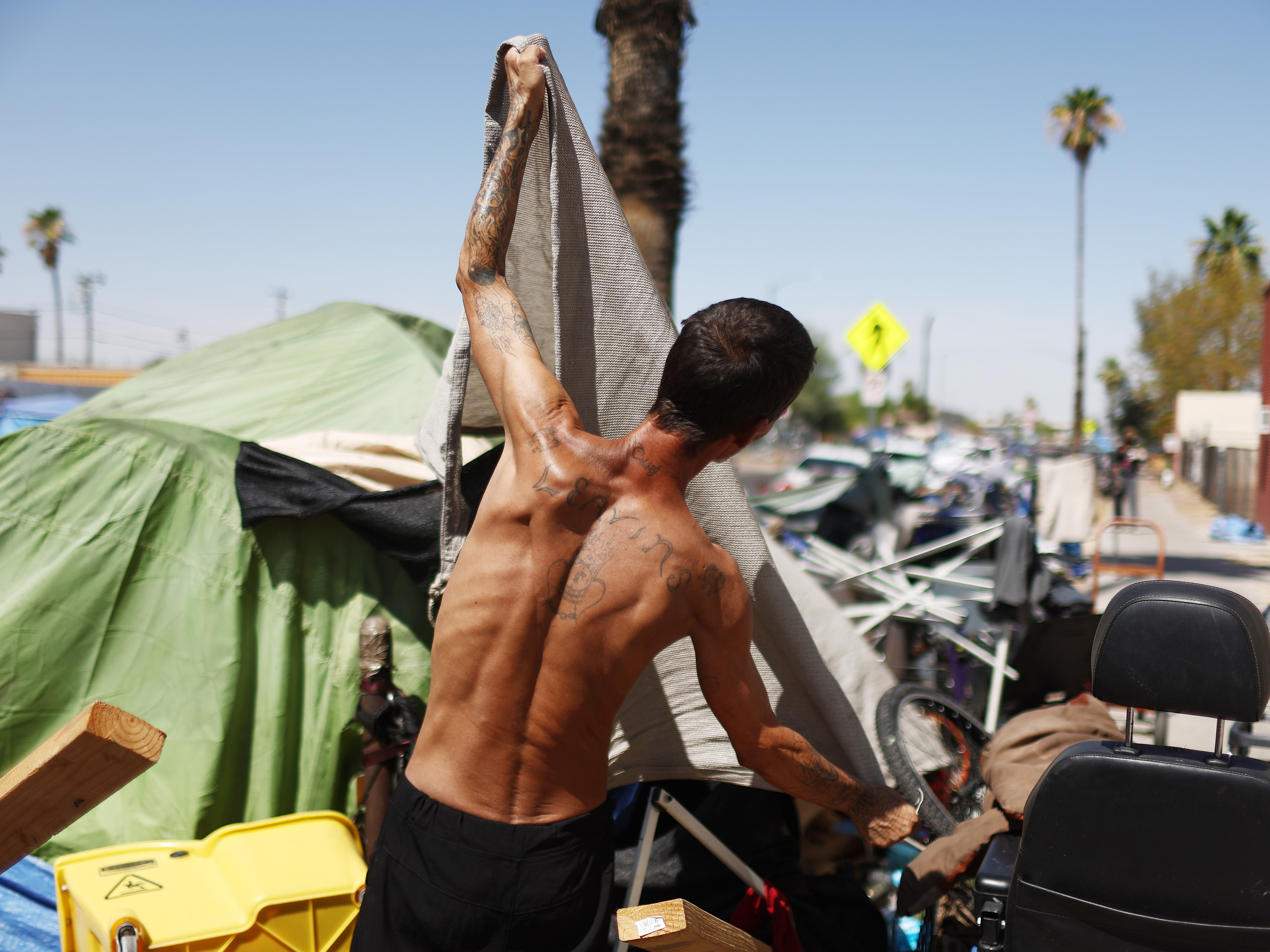 caption: A homeless person adjusts a friend's tent to help increase shade cover in a section of The Zone, Phoenix's largest homeless encampment.