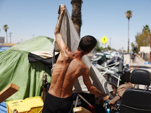 caption: A homeless person adjusts a friend's tent to help increase shade cover in a section of The Zone, Phoenix's largest homeless encampment.