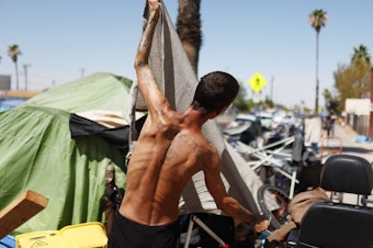 caption: A homeless person adjusts a friend's tent to help increase shade cover in a section of The Zone, Phoenix's largest homeless encampment.