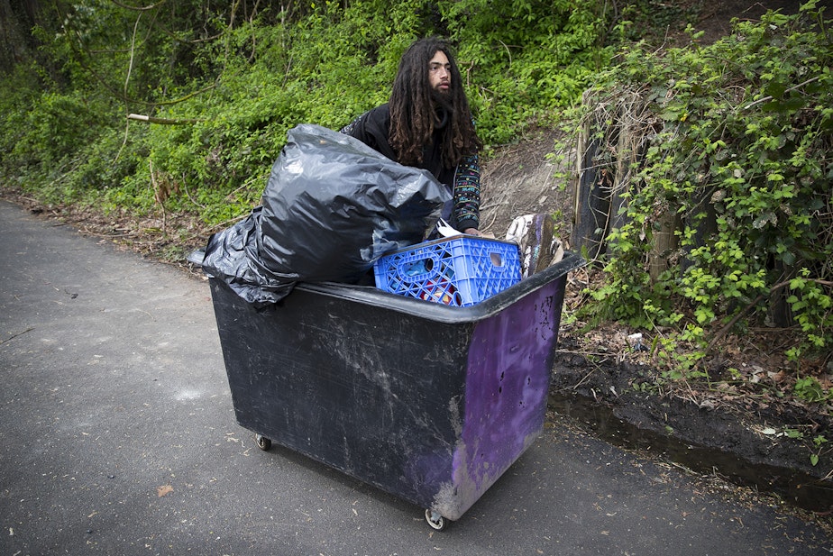 caption: Ethan Kent, 26, uses a cart to transport his belongings as well as the belongings of friends away from a Ravenna encampment where he had been living for roughly a month and a half, on Wednesday, April 18, 2018, on the Burke-Gilman Trail in Seattle.