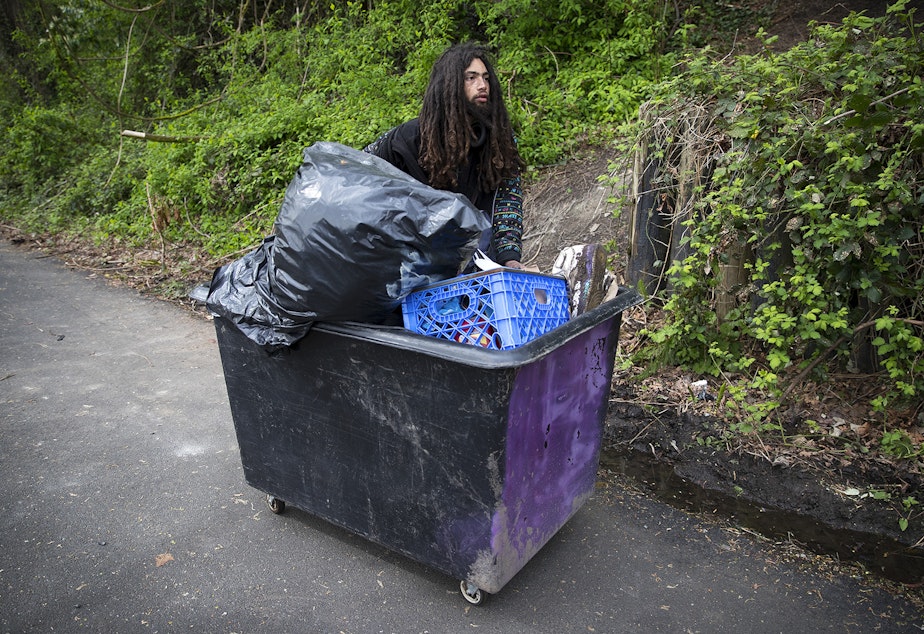 caption: Ethan Kent, 26, uses a cart to transport his belongings as well as the belongings of friends away from a Ravenna encampment where he had been living for roughly a month and a half, on Wednesday, April 18, 2018, on the Burke-Gilman Trail in Seattle.
