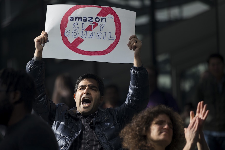 caption: Jon Mannella, center, protests Amazon dropping $1 million-plus dollars into the Seattle city council election on Thursday, October 24, 2019, during a 'Stop Bezos from Buying this Election' rally at Amazon's spheres in Seattle. 