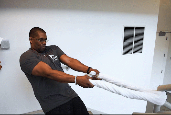 caption: Wrap a towel around a banister or column. Lean back at a 45-degree angle or more. Keep your feet planted close to the banister. The goal is to support your weight with the towel — that'll give your upper body a real workout.