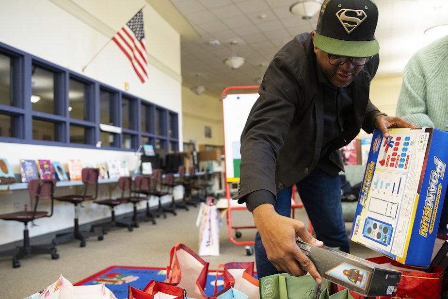 caption: Rogers Greene, a family support worker at Dunlap Elementary School, sorts gifts for students on Friday, Dec. 20, 2024, at Dunlap Elementary School in Seattle.