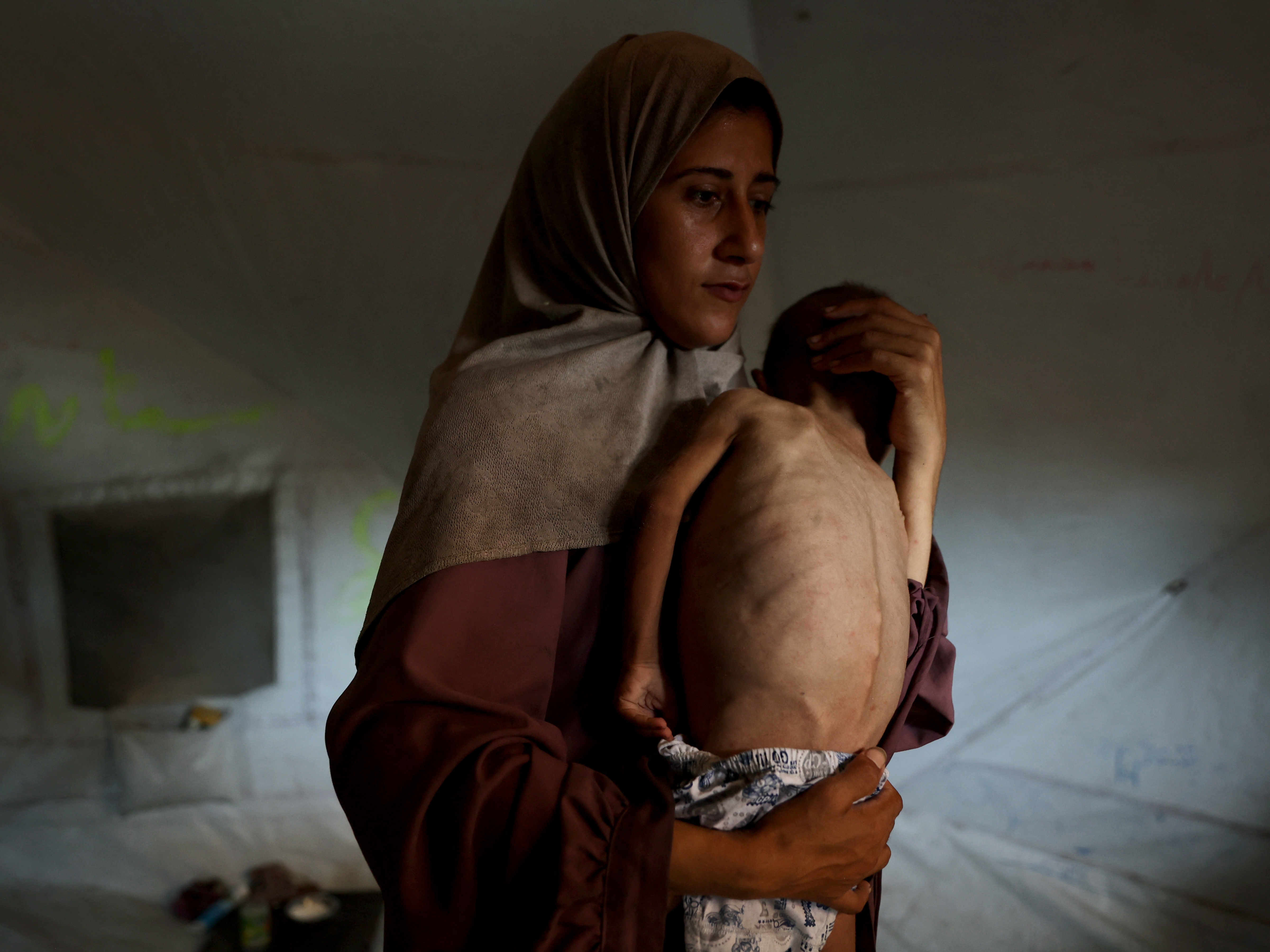 caption: Hidaya, a 31-year-old Palestinian mother, carries her sick 18-month-old son Mohammed al-Mutawaq, who is also displaying signs of malnutrition, inside their tent at the Al-Shati refugee camp, west of Gaza City, on July 24, 2025.